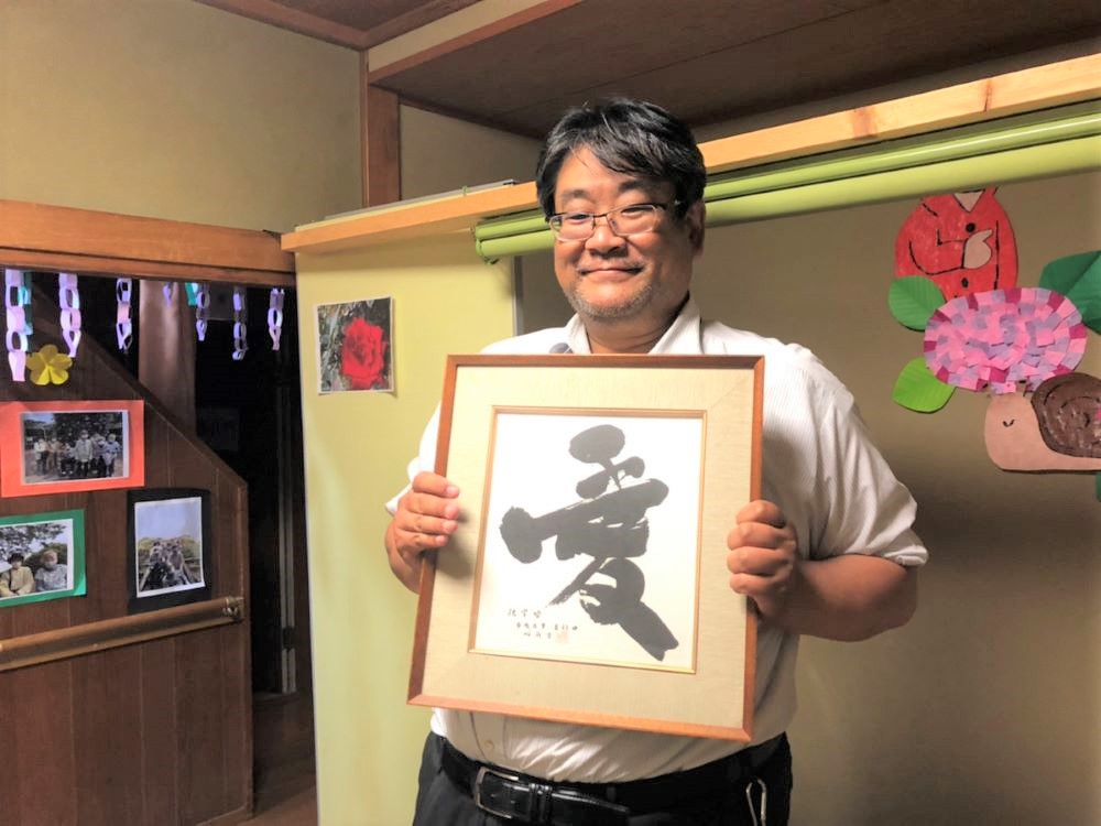 祖母の書いた「愛」の字の色紙を持ってにっこり