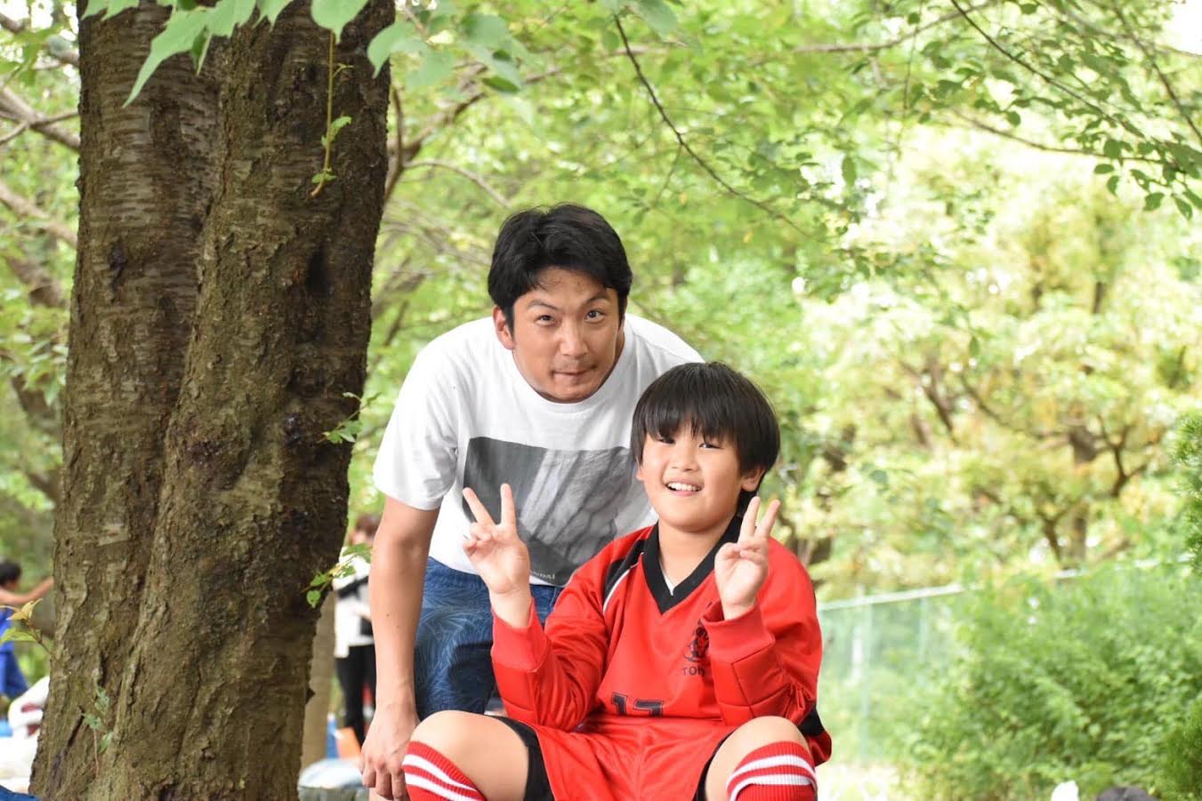 写真①サッカーユニフォーム姿の次男と
キャプ　次男と共に笑顔を見せる黒原さん　