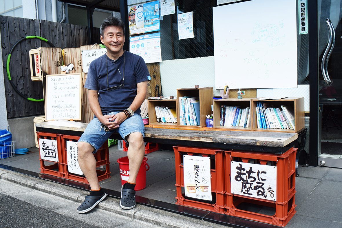 （画像１アイキャッチ兼用：「置きベン」に座る小畑さん。「人と人が〝うっかり〟つながる」と語る）
