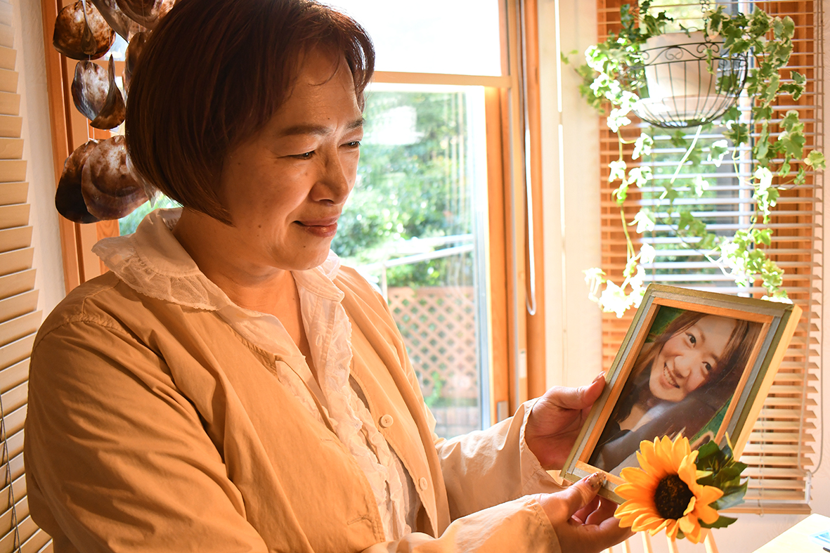 （画像１アイキャッチ兼用：娘の芳織さんの写真を手にケアについて語る佐竹美和さん）